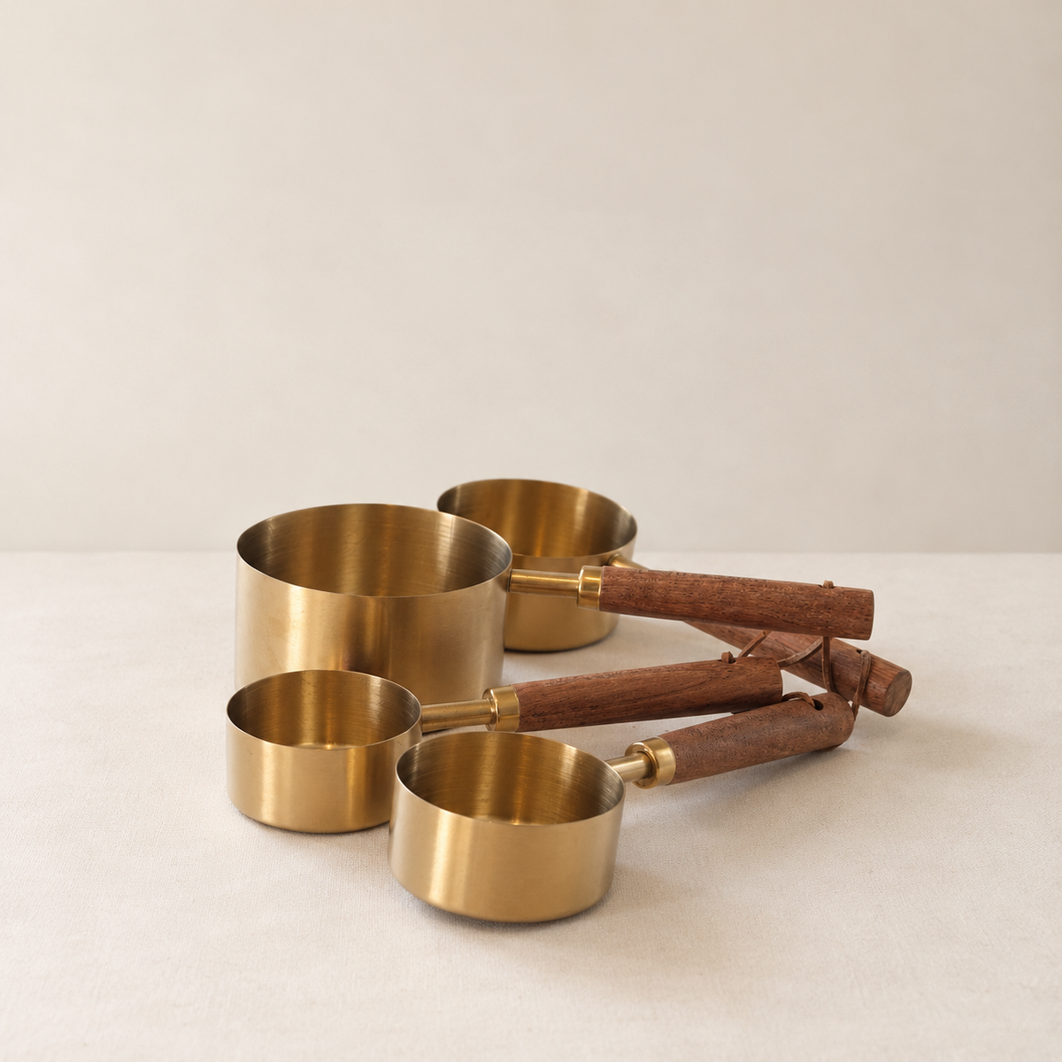 Four gold measuring cups with wooden handles on ivory background