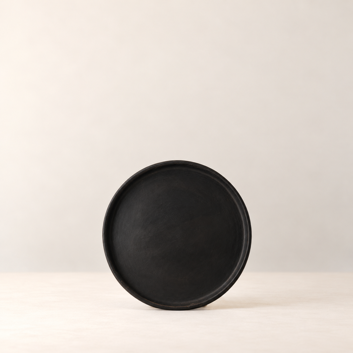 Handmade black clay plate by Rufina Ruiz López against soft ivory